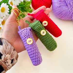 May include: Three crocheted keyrings in purple, green and red with a gold chain and ring. Each keyring has a small round button with a colourful design.
