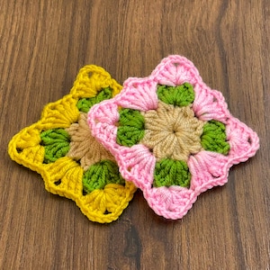 May include: Two crocheted squares, one pink and one yellow, with green accents. The squares are made with a granny stitch pattern.