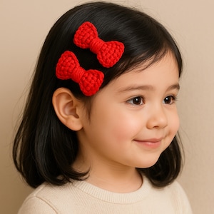 May include: Two red crocheted hair bows with a clip on the back. The bows are worn by a young girl with dark hair.