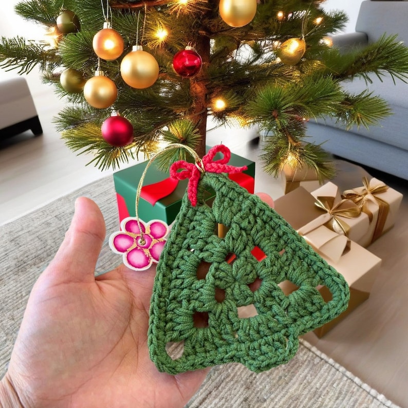 K&ouml;nnte beinhalten: Ein gr&uuml;ner geh&auml;kelter Weihnachtsbaumschmuck mit einer rosa Blumenverzierung. Der Schmuck h&auml;ngt an einem Weihnachtsbaum mit Ornamenten in verschiedenen Farben.