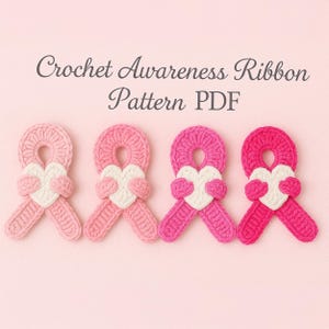 May include: Four crochet awareness ribbons in varying shades of pink, each with a white heart in the center. The ribbons are arranged in a row against a pink background. Text at the top reads "Crochet Awareness Ribbon Pattern PDF".