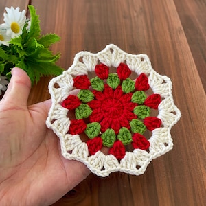 May include: A white crocheted doily with a red and green center. The doily has a scalloped edge and is made with a delicate stitch.