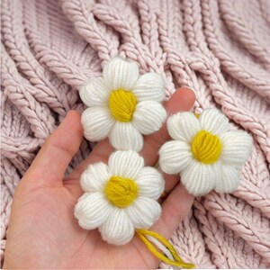 May include: Three white yarn daisies with yellow centers. The daisies are handmade and have a rustic, homemade look.
