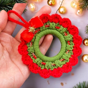 May include: A small crocheted Christmas wreath ornament with a red bow and gold accents. The wreath is green and red and has a loop for hanging.