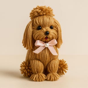 May include: A brown yarn poodle with a pink bow and a pearl accent. The poodle is sitting with its paws tucked under its body.