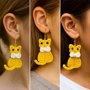 May include: Yellow crochet cat earrings with a white bow tie and black eyes. The earrings hang from gold-colored hooks. The cat design is a whimsical and handmade accessory.