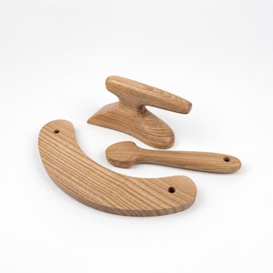 Puede incluir: Un juego de tres herramientas de costura de madera marrón claro que incluye una tabla de planchar curva con dos agujeros, un bloque de sastre con base plana y un prensador de puntas largo y delgado con extremo redondeado, con veta natural.