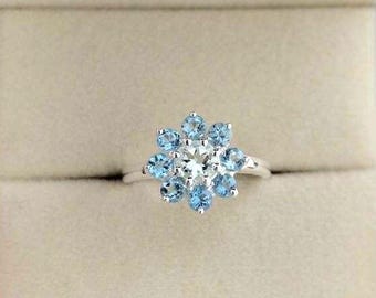 May include: A silver ring with a cluster of blue gemstones in the shape of a flower. The center stone is a clear diamond.
