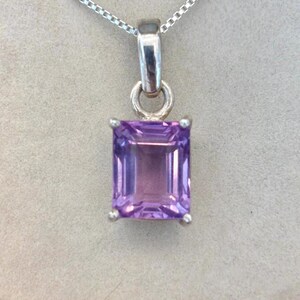 May include: A rectangular, light purple gemstone pendant with a silver chain. The gemstone is set in a silver bezel and has a faceted surface. The pendant hangs from a delicate silver chain, creating a classic jewellery piece.