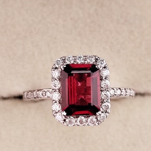 May include: A red gemstone ring with a halo of smaller diamonds. The ring is set in white gold.