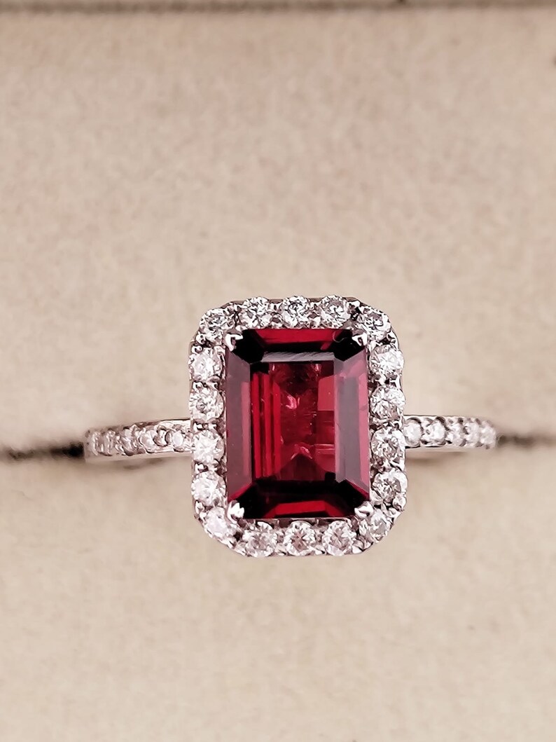 May include: A red gemstone ring with a halo of smaller diamonds. The ring is set in white gold.