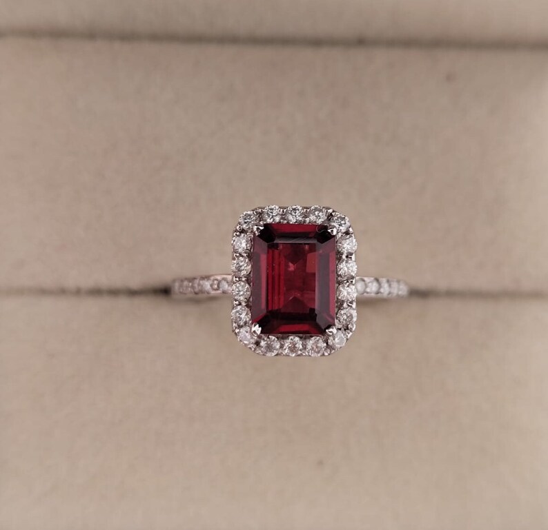 May include: A red gemstone ring with a halo of smaller diamonds. The ring is set in a silver band.