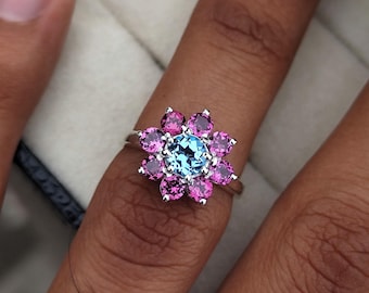 May include: A silver ring with a blue gemstone surrounded by pink gemstones.