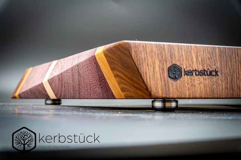 May include: A wooden cutting board with a geometric design and a dark brown finish. The board has a logo that says "kerbst&uuml;ck" and "Holz mit Geschichte".