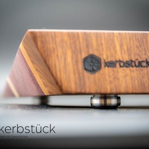 May include: A close-up of a wooden cutting board with a dark brown finish. The board has a beveled edge and a metal bearing on the bottom. The board is branded with the text "kerbst&uuml;ck" in black.