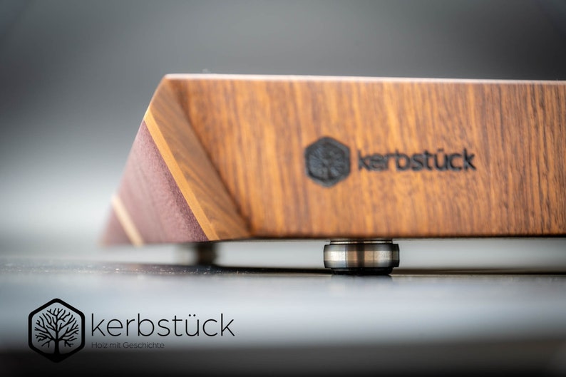 May include: A close-up of a wooden cutting board with a dark brown finish. The board has a beveled edge and a metal bearing on the bottom. The board is branded with the text "kerbst&uuml;ck" in black.