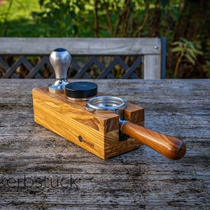 May include: A wooden coffee tamper stand with a silver tamper, a black portafilter, and a wooden handle. The stand is labeled "kerbstuck".