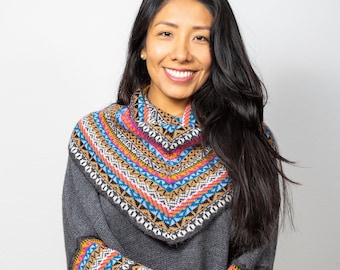 Può includere: Un poncho di maglia grigia con motivi geometrici colorati sul collo, sui polsini e sull'orlo. Il poncho ha un collo alto e una vestibilità rilassata.