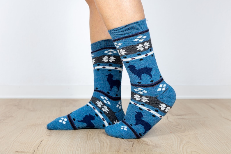 Pu&ograve; includere: Un paio di calzini blu con un motivo bianco e grigio con alpaca. I calzini sono realizzati in un materiale morbido e confortevole.