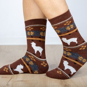 Pu&ograve; includere: Calze marroni con un motivo di alpaca bianco. Le calze hanno un design geometrico marrone, grigio e giallo.