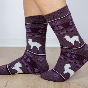 Pu&ograve; includere: Un paio di calzini viola con un design di alpaca bianco. I calzini hanno un design viola e bianco.