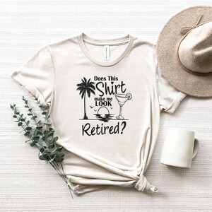 Może przedstawiać: Beżowa koszulka z czarnym nadrukiem palmy, szklanki z margaritą i tekstem "Does This Shirt Make Me Look Retired?"