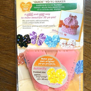 Könnte beinhalten: Ein rosa Plastik-Yo-Yo-Maker in Form eines Schmetterlings. Der Maker ist so konzipiert, dass er 3D-Yo-Yos mit einer fertigen Größe von 3 cm x 4 cm erstellt. Die Verpackung enthält Anweisungen und zeigt Beispiele für fertige Yo-Yos.