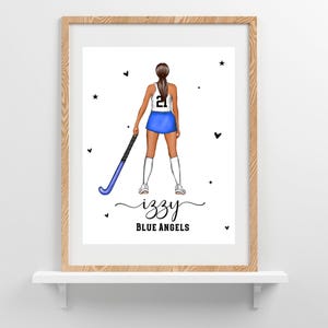 Puede incluir: Impresión enmarcada con una ilustración de dibujos animados de una jugadora de hockey sobre hierba con uniforme azul y blanco, sosteniendo un palo de hockey azul. La impresión incluye el nombre "Izzy" y el texto "Blue Angels".