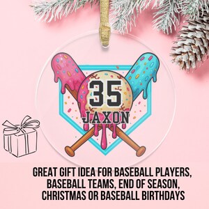 May include: A clear, round ornament with a baseball theme. It features a baseball diamond design with crossed bats and the number 35. The name "Jaxon" is below the number. The ornament has a gold ribbon for hanging.