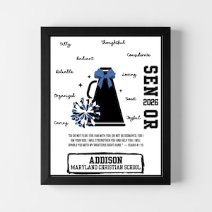 May include: Framed print with a black border, showcasing a cheerleader's megaphone with a blue bow and pom-pom. The word "Senior" is displayed vertically, with the year 2026. Includes inspirational text and school name.