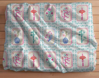 May include: A white blanket with a repeating pattern of watercolor illustrations. Each square features a different design, including dragons, fans, flowers, and vases. The illustrations are framed in pink and set against a teal grid.