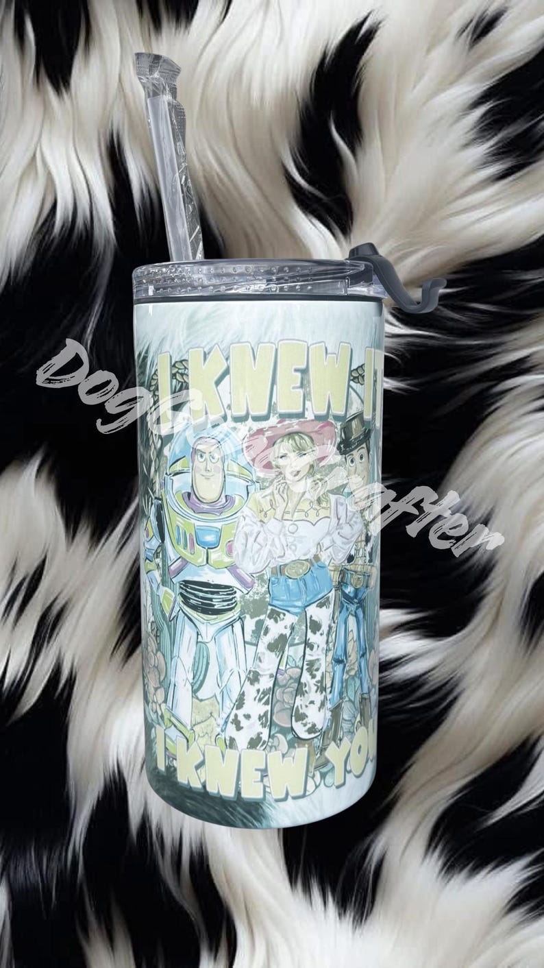 K&ouml;nnte beinhalten: Ein zylindrischer Becher mit transparentem Kunststoffdeckel und Strohhalm, der einen farbenfrohen Grafikdruck von Buzz Lightyear, Jessie und Woody aus Toy Story zeigt. Der Text "I KNEW IT" ist oben und unten in Gelb aufgedruckt.