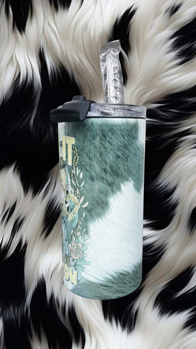 K&ouml;nnte beinhalten: Ein zylindrischer Edelstahlbecher mit einem gr&uuml;n-wei&szlig;en Kuhfellmuster. Das Design zeigt eine Zeichentrickfigur, florale Akzente und den Teiltext IT und COW. Er verf&uuml;gt &uuml;ber einen transparenten Deckel mit einem schwarzen Schiebeverschluss.