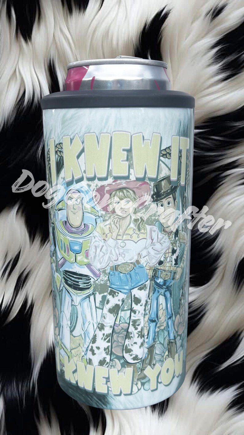 K&ouml;nnte beinhalten: Ein zylindrischer Dosenk&uuml;hler aus Metall mit einem Grafikdruck von drei animierten Figuren, darunter ein Weltraum-Ranger, ein Cowgirl und ein Cowboy. Der Text "I KNEW IT" steht oben und "KNEW YOU" unten in hellgelber Schrift.