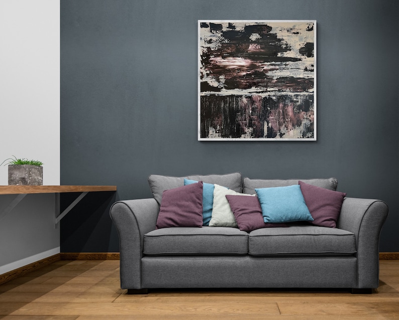 Może przedstawiać: Szara,  tkana sofa z czterema poduszkami w r&oacute;żnych odcieniach fioletu, niebieskiego i białego. Sofa stoi przed ciemnoszarą ścianą z abstrakcyjnym obrazem w ramie nad nią.