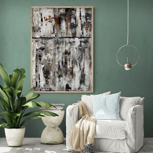 Op de afbeelding: Een witte fauteuil met een lichtblauw kussen en een beige deken. De fauteuil staat voor een groene muur met een ingelijst abstract schilderij in zwart, wit en bruine tinten. Een gouden ring hanglamp hangt aan het plafond.
