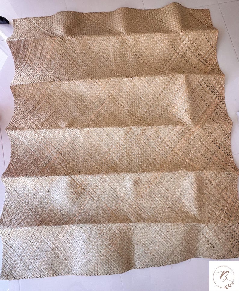 May include: A woven mat made of natural fibers, featuring a light brown color and a textured, rectangular design. The mat is folded in a zig-zag pattern, creating a layered effect. The mat is likely used for decorative or functional purposes.