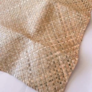May include: Close-up of a woven mat made from natural fibers. The mat has a square pattern and a light brown color. The texture is visible, showing the individual strands of the material. The mat is folded, creating soft curves.