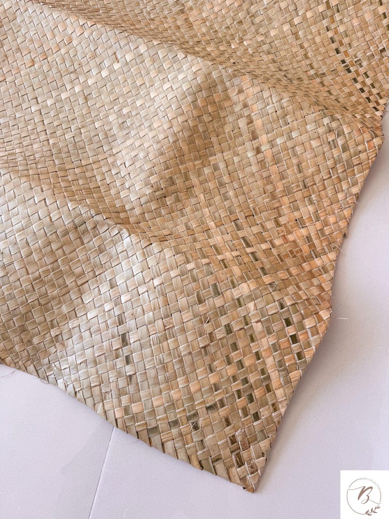 May include: Close-up of a woven mat made from natural fibers. The mat has a square pattern and a light brown color. The texture is visible, showing the individual strands of the material. The mat is folded, creating soft curves.