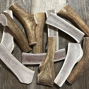 May include: A collection of various sizes and shapes of natural antler dog chews. The chews are a light brown color with a white, textured surface.