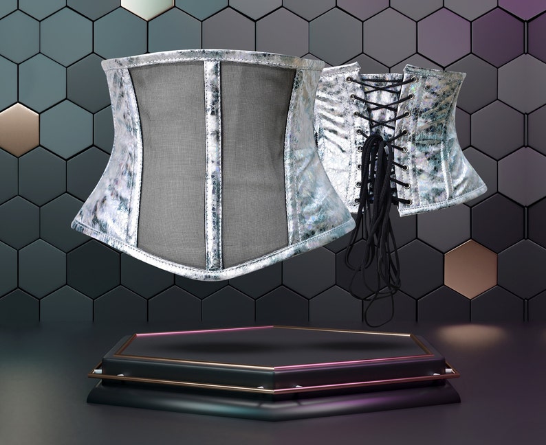 K&ouml;nnte beinhalten: Zwei silberne Korsetts mit schwarzen Schn&uuml;rdetails auf einem schwarzen sechseckigen Hintergrund. Die Korsetts stehen auf einem schwarzen sechseckigen Sockel mit goldenen und rosafarbenen Akzenten.