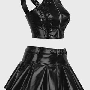 May include: A black faux leather two-piece set consisting of a sleeveless crop top and a pleated mini skirt. The top features a high collar with a buckle, a front zipper, and side lace-up details. The skirt includes a matching belt at the waist.
