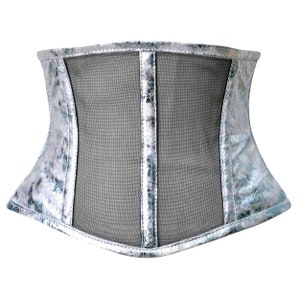 K&ouml;nnte beinhalten: Ein silbernes Korsett mit einem Mesh-Panel an der Vorderseite. Das Korsett hat ein gl&auml;nzendes, irisierendes Finish.