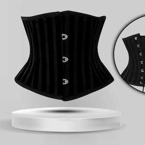 May include: Black corset with vertical stripes and silver metal clasps. The corset is on a white pedestal.
