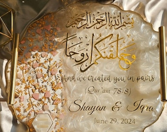 May include: A round, white and translucent resin tray with gold metal handles, featuring gold calligraphy, the text "And we created you in pairs (Qur'am 78:8)", "Shayan & Iqra", and "June 29, 2024". The tray includes gold leaf flakes and pink stone chips.