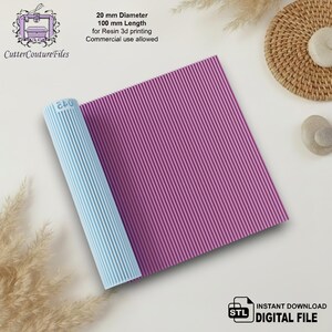 Puede incluir: Una hoja rectangular texturizada de color púrpura con un patrón de costillas verticales repetitivo y un rodillo cilíndrico azul claro con un patrón de costillas verticales y el texto 045. El texto indica 20 mm de diámetro, 100 mm de longitud para impresión 3D en resina.
