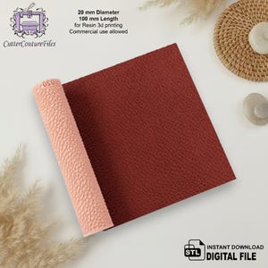 Puede incluir: Un rodillo cilíndrico para impresión 3D con superficie texturizada, que mide 20 mm de diámetro y 100 mm de longitud. El rodillo es de color melocotón claro y se muestra junto a una muestra cuadrada de material rojo oscuro con textura en relieve.