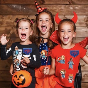 Può includere: Tre bambini vestiti con costumi di Halloween. Un bambino indossa un costume da strega con un cappello a punta bianco e nero. Un altro bambino indossa un costume da diavolo con corna rosse e un mantello rosso. Il terzo bambino indossa un costume da scheletro nero con un secchiello di zucca. Tutti e tre i bambini sorridono e tengono in mano vari oggetti di scena di Halloween. I bambini indossano toppe che recitano "Good Guys" sui loro costumi.