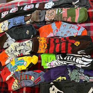 May include: A collection of colorful socks featuring various horror movie characters. The socks are displayed on a red and black plaid surface.