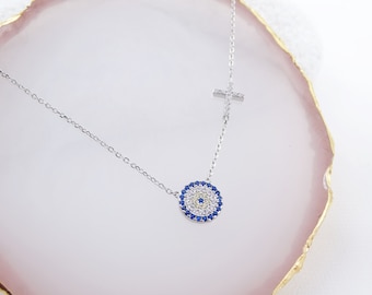 May include: A silver necklace with a blue and white evil eye charm and a small silver cross pendant.